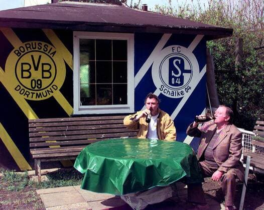 Zwei Fußballfans, li. Udo von Harzer Radlitz (BVB Fanoriginal), bei einer Flasche Bier im Gespräch vor einer Gartenlaube, die mit Logos der verfeindeten Mannschaften BVB (li.) und Schalke geziert ist Fußball 1. BL Herren Saison 1997 1998, BVB Borussia Dortmund FC Schalke 04 Fanoriginal, Fanleben, Fankult Totale Fanleben Fanfreundschaft Freundschaft Dortmund Vdia quer Harmonie