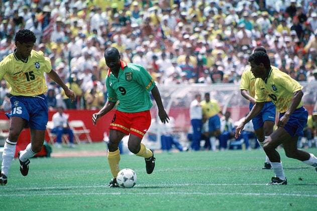Der Kameruner Roger Milla mit Ball, verfolgt vom Brasilianer Marcio Santos (li.), re. Aldair Fußball WM Herren Länderspiel, Weltmeisterschaft 1994: Brasilien - Kamerun Gruppe San Francisco Dynamik,