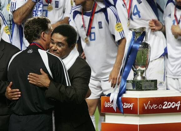 Portugals Fußballlegende Eusebio umarmt Trainer Otto Rehhagel (li., Griechenland) bei der Siegerehrung, der Coach riskiert schon einen Blick auf den Pokal der Euro 2004 Fußball EM Herren Europameisterschaft, Euro 2004, Länderspiel, Nationalmannschaft, Nationalteam, Finale, Endspiel Gruppe Lissabon Harmonie,