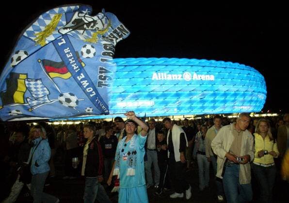 Die Fans von 1860 verlassen fahnenschwenkend die blau leuchtende Allianz Arena - MODEL RELEASED Fußball 2. BL Herren Saison 2004 2005, Eröffnungsspiel, Eröffnung, Test, Testspiel, Stadioneröffnung, Einweihung Totale AllianzArena, Beleuchtung, beleuchten, nachts München Symbol