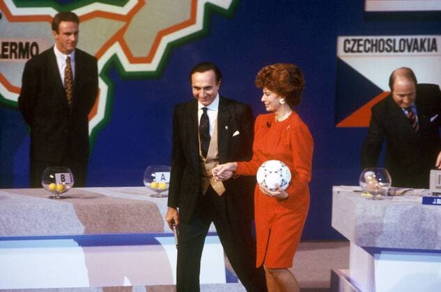 Auslosung zur WM 1990: die Schauspielerin Sophia Loren (Italien) schreitet elegant an der Hand des Moderators über die Bühne, im Hintergrund stehen Karl Heinz Rummenigge (li., BRD) und FIFA Generalsekretär Sepp Blatter (Schweiz) vor den Lostöpfen Fußball WM Herren Vorschau 1989 Weltmeisterschaft 1990, Gruppenauslosung, Vdia Gruppe Rom