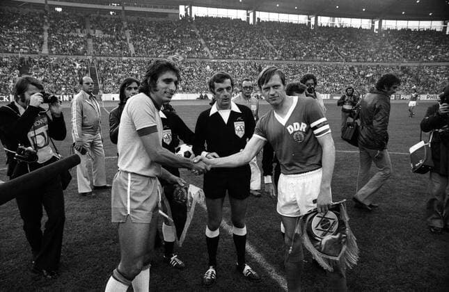 Mario Marinho Peres (Brasilien, li.) und Bernd Bransch (DDR, re.) bei der Begrüßung, FIFA Schiedsrichter John Thomas (Wales) schaut zu Fußball WM Herren Weltmeisterschaft 1974, Nationalmannschaft, Nationalteam, Nationaltrikot, Länderspiel, Zwischenrunde Gruppe Hannover