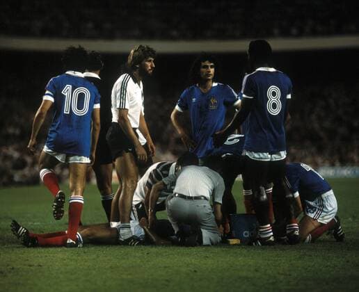 Michel Platini (Frankreich, Mitte) und Manfred Kaltz (beide BR Deutschland, 2.v.li.) schockiert wegen der Verletzung von Patrick Battiston (Frankreich, am Boden) nach dessen Zusammenstoß mit Torwart Harald Schumacher (BR Deutschland, nicht im Bild) - DEUTSCHSPRACHIGE SPORTZEITSCHRIFTEN UND -ZEITUNGEN NUR NACH RÜCKSPRACHE Fußball Länderspiel Herren WM 1982, Nationalteam, Halbfinale, Nationaltrikot, BRD, BR Deutschland - Frankreich 8:7 n.E. Gruppe Sevilla