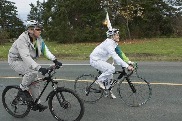 Flanked by a VANOC volunteer the 54th torch bearer, Olympic cyclist Errine Willock (R) rides her leg of the relay on the first day of the 2010 Winter Olympic Torch Relay -  VIC2009103028 o0 Fackelläufer, Fackelläufer o00 Olympiafeuer