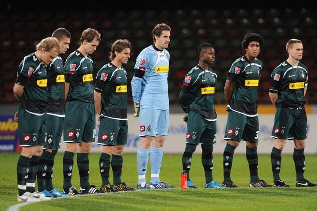 Gladbachs Spieler während der Gedenkminute zu Ehren des verstorbenen Torwart Robert Enke (Hannover 96), v.li. Tobias Levels (Borussia Mönchengladbach), Roman Neustädter (Borussia Mönchengladbach), Thomas Kleine (Borussia Mönchengladbach), Marcel Meeuwis (Borussia Mönchengladbach) und Torwart Christofer Heimeroth (Borussia Mönchengladbach), Moses Lamidi (Borussia Mönchengladbach), Bonfim Dante (Gladbach) und Filip Daems (Borussia Mönchengladbach) o0 Tod tot Todesfall Trauer trauern Schweigeminute Gedenken Andenken schweigen pessimistisch o0 Gladbach