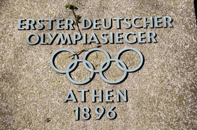 Gedenkstein für den ersten Deutschen Olympiasieger in einer Einzeldisziplin, Carl Schuhmann, bei den ersten Olympischen Spielen der Neuzeit 1896 in Athen. auf dem Gelände des Olympischen Dorfes von 1936 in Elstal (Havelland). Er gewann die Goldmedaille im Pferdsprung. Die ehemalige Grabplatte ist ein Geschenk seines Enkels an die Besucher des Olympischen Dorfes. o0 Objekte Turnen Geräteturnen Sieg Herren