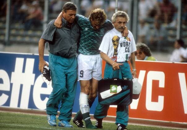 Der verletzte Rudi Völler wird von Mannschaftsarzt Prof. Dr. Heinrich Heß (li.) und Physiotherapeut Adolf Katzenmaier (alle BR Deutschland) gestützt - DEUTSCHSPRACHIGE SPORTZEITSCHRIFTEN UND -ZEITUNGEN NUR NACH RÜCKSPRACHE Fußball WM Herren WM Halbfinale 1990, Länderspiel, Nationalteam, Nationaltrikot, BRD Gruppe Turin