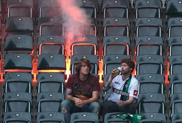 02.10.2010, Gladbach, Deutschland, 1.Fussball Bundesliga - Saison 2010 2011, Borussia Mönchengladbach, Zwei Gladbacher Fans sitzen vor einer Leuchtfakel o0 Fan, Fußballfan, Publikum bengalische Feuer Bengalfeuer Rauch Qualm Feuer kurios Komik