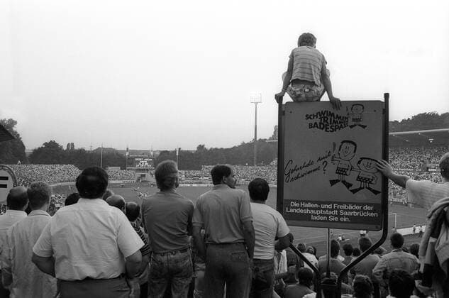 Fußball, Stadiongeschichte 1. FC Saarbrücken Zuschauer im Saarbrücker Ludwigsparkstadion, Heimspielstätte des 1. FC Saarbrücken, neben einem Werbeplakat für die Saarbrücker Hallenbäder und Freibäder Aufnahmedatum geschätzt, 1989 Saarbrücken, Deutschland, Ludwigspark