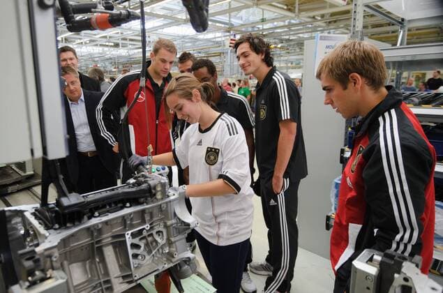 Eine Mitarbeiterin von Mercerdes-Benz zeigt den Spielern der Nationalmannschaft ihre Arbeit am Band. v.l. Torwart Manuel NEUER, CACAU, Mats HUMMELS, Philipp LAHM. Werksführung der deutschen Fussball Nationalmannschaft im Motorenwerk von Mercedes-Benz in Bad Cannstatt Stuttgart am 9.8.2011. o00 Wirtschaft Fan