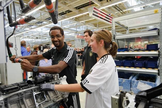 CACAU (GER) l. laesst sich die Fertigung am Band von einer Mitarbeiterin erklaeren und legt selber Hand an. Werksführung der deutschen Fussball Nationalmannschaft im Motorenwerk von Mercedes-Benz in Bad Cannstatt Stuttgart am 9.8.2011. o00 Wirtschaft Fan
