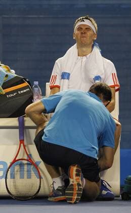 Australian Open 2012, Melbourne Park,ITF Grand Slam Tennis Tournament,Cedrik-Marcel Stebe (GER) mit Schmerz verzerrtem Gesicht während er vom Physiotherapeuten behandelt wird, Verletzung,Ganzkoerper,Hochformat,