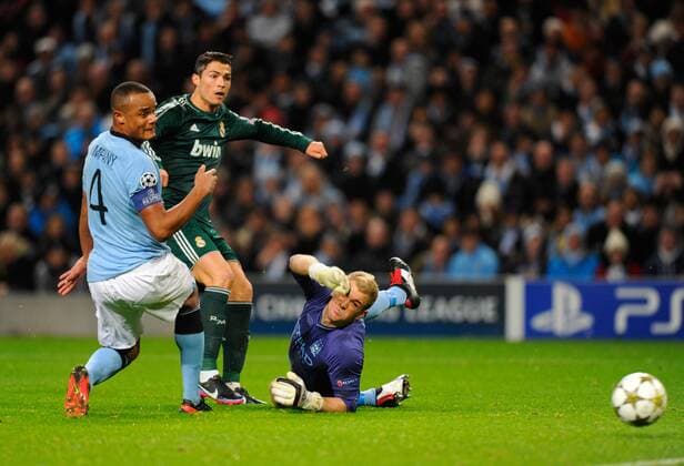 Cristiano Ronaldo of Real Madrid gets his shot away between Vincent Kompany of Manchester City and Joe Hart of Manchester City - UEFA Champions League Group D - Manchester City vs Real Madrid - Etihad Stadium - Manchester - 21 11 12 - - EDITORIAL USE ONLY. No use with unauthorised audio, video, data, fixture lists, club league logos or live services. Online in-match use limited to 120 images, no video emulation. No use in betting, games or single club league player publications.