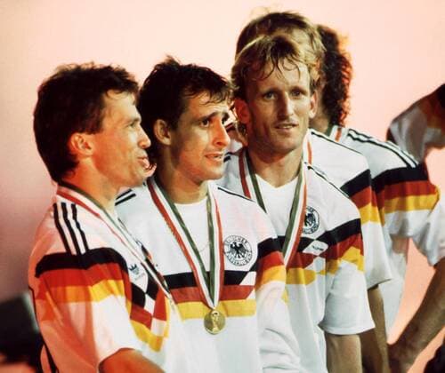 Durch einen verwandelten Foulelfmeter von Andreas Brehme sicherte sich die DFB-Auswahl am 8. Juli 1990 im Olympiastadion von Rom den dritten Weltmeistertitel für den Deutschen Fußball Bund. Abgekämpft aber glücklich die Deutschen Spieler nach der Übergabe der Medaillen. Von links: Torschütze Andreas Brehme, Pierre Littbarski und Lothar Matthäus.