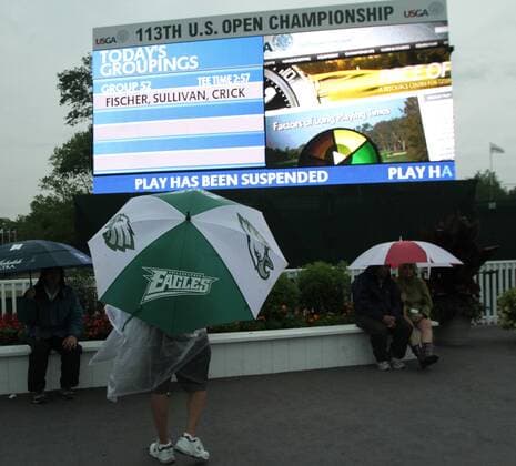 June 13 2013: Fan takes cover under a Philadelphia Eagles umbrella and watches the large scoreboard announcing suspended play as morning storms cause a rain delay on the first round at the 2013 U.S. Open hosted by Merion Golf Club in Ardmore, PA. GOLF: JUN 13 PGA Golf Herren - U.S. Open - First Round Icon1306130331 EDITORIAL USE ONLY