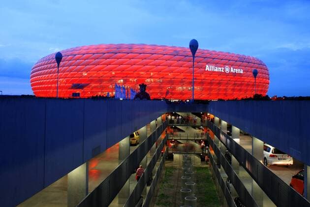 in den Farben des FC Bayern München s erleuchtete Fassade der Allianz Arena mit Tiefgarage in der Abenddämmerung