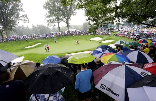 Spectators watch the action on the 13th green while holding umbrellas in the rain in the second round of the PGA Golf Herren Championship at Oak Hill Country Club in Rochester, New York on August 9, 2013.  NYP20130809123