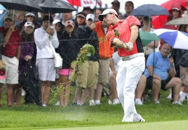 Spectators watch while holding umbrellas in the rain as Rory McIlroy hits a shot out of the rough to the 18th green in the second round of the PGA Golf Herren Championship at Oak Hill Country Club in Rochester, New York on August 9, 2013.  NYP20130809104
