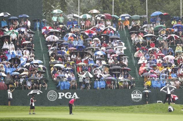 Spectators watch while holding umbrellas in the rain as Miguel Angel Jimenez putts on the 18th green in the second round of the PGA Golf Herren Championship at Oak Hill Country Club in Rochester, New York on August 9, 2013.  NYP20130809105