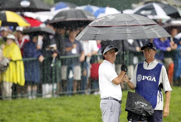 Phil Mickelson and caddie Jim Bones MacKay react under an umbrella in the rain on the 14th tee box in the second round of the PGA Golf Herren Championship at Oak Hill Country Club in Rochester, New York on August 9, 2013.  NYP20130809119