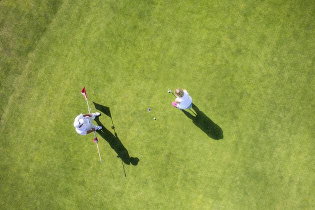 Zwei Golfspieler auf einem Grün, Spielerin beim putten, einlochen des Golfballs.