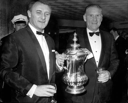 Chelsea Manager Tommy Docherty (left) and Tottenham Hotspur Manager Bill Nicholson hold the Football Association Cup between them and wonder which of them will be holding it after Saturday s FA Cup final between the two teams at Wembley. They are seen at the Boxing Dinner Evening in honour of the Chelsea and Spurs finalists in the London Hilton. 15th May 1967.  UnitedArchives00455488