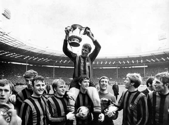26th April 1969: The FA cup final at Wembley, Manchester City versus Leicester City. Photo shows: Captain, Tony Book holds aloft the trophy as he is chaired around Wembley Stadium by his team mates. (l-r) David Connor; Tommy Booth; Glyn Pardoe; Francis Lee; Mike Doyle (supporting Book on his shoulders), goalkeeper, Harry Dowd; Colin Bell and Alan Oakes.  UnitedArchives01009474