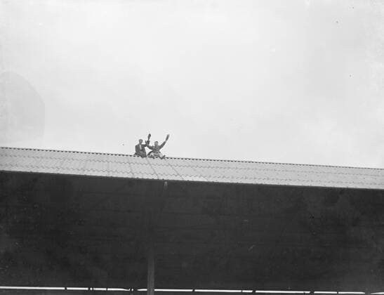 Football match : Arsenal Football Club versus Charlton Athletic Football Club at Highbury Stadium , London . Onlookers sit on the roof of the stand . 1936  UnitedArchives01578400