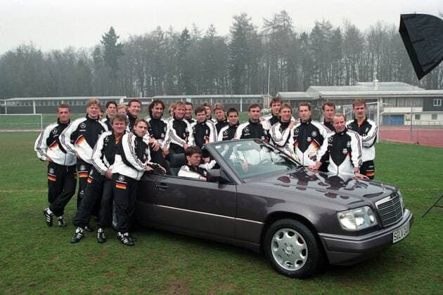Die Nationalmannschaft posiert vor einem Mercedes: hi.v.li: Thomas Strunz, Stefan Effenberg, Mehmet Scholl, Christian Ziege, Matthias Sammer, Guido Buchwald, Maurizio Gaudino, Jürgen Klinsmann (verdeckt), Andreas Brehme, Jürgen Kohler, Andreas Möller, Thomas Helmer, Christian Wörns, Ulf Kirsten, Stefan Kuntz, Bodo Illgner, Andreas Thom, Andreas Köpke, Co-Trainer Rainer Bonhof, Bundestrainer Berti Vogts, Mario Basler; vor dem Wagen: Torwarttrainer Sepp Maier (li.) und Thomas Häßler; im Wagen: Lothar Matthäus