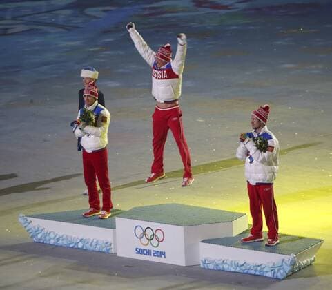 Russia s Alexander Legkov (C) leaps into the air as he is announced as the gold medal winner for the men s 50km cross-country skiing mass start race during the Closing Ceremony at the Sochi 2014 Winter Olympics on February 23, 2014 in Sochi, Russia. With Legkov on the podium are teammates Maxim Vylegzhanin (L) who won silver and Ilia Chernousov who won bronze in the race.  OLY20140223130
