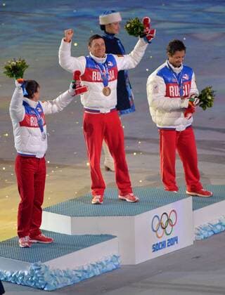 Russia s Alexander Legkov (C) celebrates his gold medal for the men s 50km cross-country skiing mass start race during the Closing Ceremony at the Sochi 2014 Winter Olympics on February 23, 2014 in Sochi, Russia. With Legkov on the podium are teammates Maxim Vylegzhanin (L) who won silver and Ilia Chernousov who won bronze in the race.  OLY20140223145