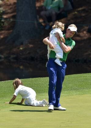 Luke Donald picks up his daughter Sophia Ann as his other daughter Elle crauls away not the eighth green during the Par 3 Contest during the Masters Tournament at Augusta National Golf Club in Augusta, Georgia, April 8, 2014.  AUG20140409361