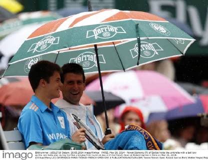 PARIS, May 26, 2014 - Novak Djokovic (R) of Serbia holds the umbrella with a ball boy as the rain halts play during his Men s Singles first round on day 2 of the French Open at Roland Garros in Paris on May 26, 2014. (Xinhua Wang Lili) (SP)FRANCE-PARIS-TENNIS-FRENCH OPEN-DAY 2 