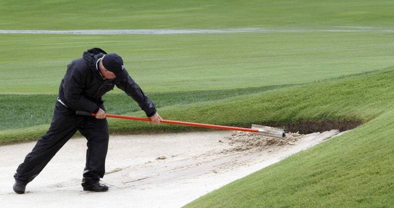 A groundskeeper rakes sand eroded from a greenside bunker on the ninth hole after a thunderstorm forced a suspension in play of the final round of the 96th PGA Golf Herren Championship at Valhalla Country Club on August 10, 2014 in Louisville, Kentucky.  LOU2014081003