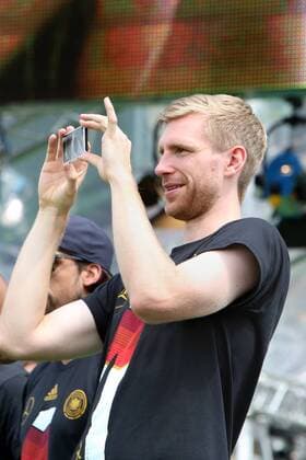 Berlin-Mitte: Fanfest auf der Straße des 17. Juni vor dem Brandenburger Tor anlässlich der FIFA Fußball WM 2014 in Brasilien. - Empfang der Weltmeister - Per Mertesacker beim Fotografieren mit seinem Smartphone auf der Bühne
