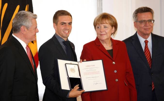 10.11.2014, Berlin, Verleihung des Silbernen Lorbeerblattes an die Spieler der Fußball-Nationalmannschaft durch den Bundespräsidenten Joachim Gauck im Schloss Bellevue. Bild: Bundespräsidenten Joachim Gauck, Bundeskanzlerin Angela Merkel und Thomas de Maiziere übereichen Philipp Lahm das Silberne Lorbeerblatt für die Mannschaft Verleihung des Silbernen Lorbeerblattes an die Spieler der Fußball-Nationalmannschaft
