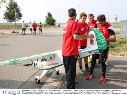 Josef Schmidt (Rasenhelfer des FC Augsburg) und Hobby-Flugzeugmodell-Bauer hat ein FCA-Flugzeug konstruiert. Spieler signieren auf dem Höhenruder, (v.li.) Josef Schmidt, Paul Verhaegh, Sascha Mölders, Halil Altintop, FC Augsburg, Training, Saison 2015 - 2016, 11.08.2015