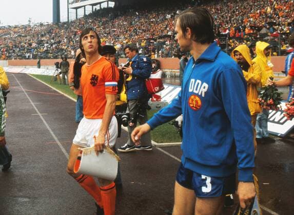 Football - 1974 World Cup - Second Round, Group 2: Holland 2 East Germany (DDR) 0 Holland s captain Johan Cruyff walks out with East Germany captain Bernd Bransch at the Parkstadion, Gelsenkirchen. 30 06 1974 