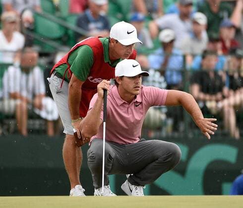 Brooks Koepka (R) gets some help from his caddie Richard Elliot as he lines up his putt on the 18th green during round 3 of the 117th U.S. Open golf tournament at Erin Hill golf course on June 17, 2017 in Erin, Wisconsin.  BK18807 BRIANxKERSEY
