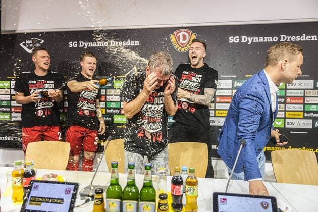 Fußball, 2. Bundesliga, Saison 2017 2018, SG Dynamo Dresden, 32. Spieltag, SG Dynamo Dresden - Fortuna Düsseldorf (28.04.2018), DDV - Stadion, Dresden. Düsseldorfs Trainer Friedhelm Funkel wird von seinen Spielern nach dem Aufstieg in die Bundesliga während der Pressekonferenz mit Bier geduscht. Dynamos Pressesprecher Henry Buschmann (re.) verlässt das Podium. *** Football 2 Bundesliga Season 2017 2018 SG Dynamo Dresden 32 Matchday SG Dynamo Dresden Fortuna Dusseldorf 28 04 2018 DDV Stadion Dresden Dusseldorf coach Friedhelm Funkel is showered with beer by his players after the promotion to the Bundesliga during the press conference Dynamos press officer Henry Buschmann re leaves the podium RM001
