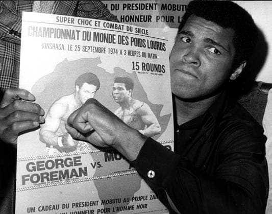 MUHAMMAD ALI THROWS A PUNCH AT GEORGE FOREMAN IN A POSTER DURING A STOP AT ORLY AIRPORT WHILE HE WAS ENROUTE TO KINSHASA,ZAIRE FOR HIS UPCOMING CHAMPIONSHIP HEAVYWEIGHT FIGHT AGAINST WORLD HEAVYWEIGHT CHAMPION GEORGE FOREMAN 9 23. ALI TOLD NEWSMEN HE PREDICTED BE MAY SNATCH A FIRST-ROUND VICTORY IN THIS FIGHT SCHEDULED 15 ROUNDS. .HPT WST BELGA  x85197328stx