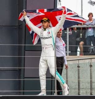 14th July 2019; Silverstone Circuit, Northampton, England; FIA F1 Grand Prix of Britain, Race Day; Mercedes AMG Petronas Motorsport driver Lewis Hamilton waves a Union Jack flag as he walks onto the podium  ActionPlus12153798 TimxWilliams