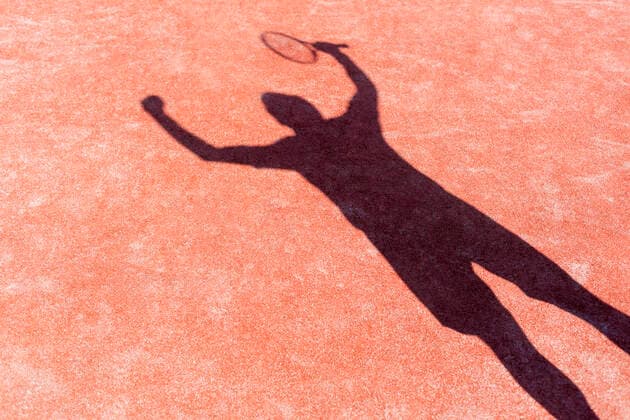 Shadow of successful man standing with arms raised on red tennis court during match INH_19064_13245