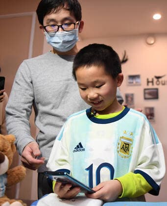 (200316) -- CHANGSHA, March 16, 2020 -- Lu Shu (R) and his father Lu Xin have a video chat with Wu Yu at home in Changsha, central China s Hunan Province on March 16, 2020. Wu Yu is a nurse from the third batch of medical teams from Xiangya Hospital to the coronavirus-hit Hubei Province. After a busy day on duty on March 8, Wu was asked if she had a wish for Women s Day, and gave what she felt was an ambitious response. I believe a jersey from Messi would definitely encourage my boy to become a member of the national youth training team, she said. The official Weibo account of Argentina s national football team responded on the very night and sent the gift to Lu Shu on March 16 to make her wish come true. ) (SP)CHINA-CHANGSHA-COVID-19-MESSI S JERSEY (CN) XuexYuge 