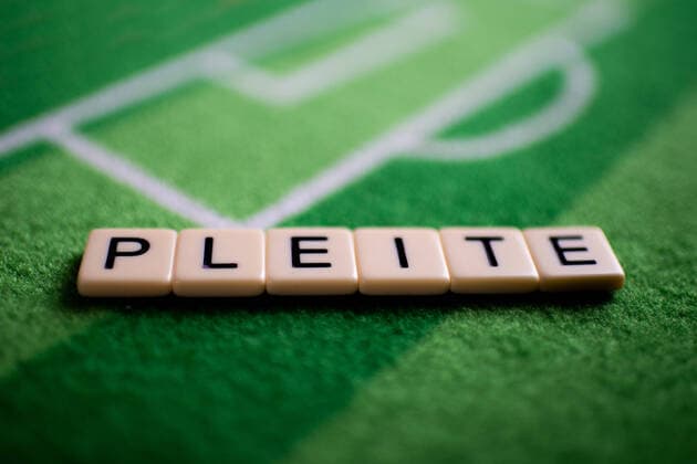 The corona virus Covid 19 causes event cancellations of, for example, football matches of Bundesliga professionals for an indefinite period of time and many effects, in the picture The word bankruptcy on a football carpet Germany