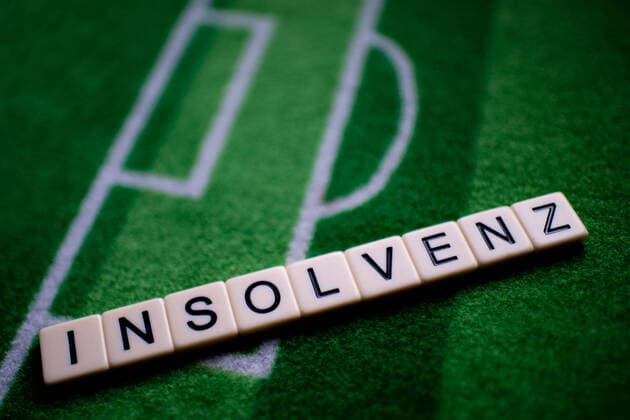 The corona virus Covid 19 causes event cancellations of, for example, football matches of Bundesliga professionals for an indefinite period of time and many effects, in the picture The word insolvency on a football carpet Germany