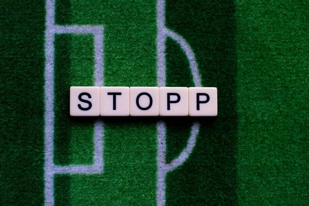 The corona virus Covid 19 causes event cancellations of, for example, football matches of Bundesliga professionals for an indefinite period of time and many effects, in the picture The word stop on a football carpet Germany