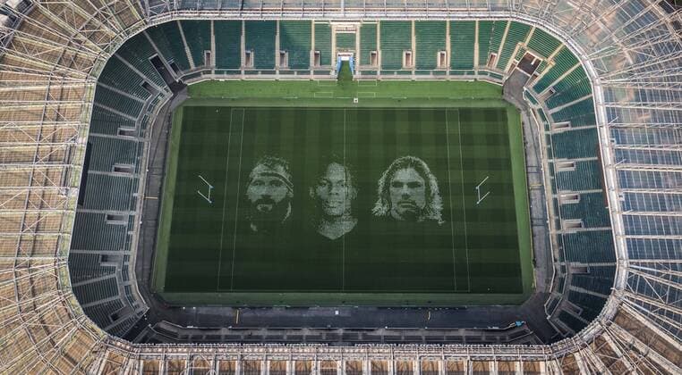 The pitch at Twickenham Stadium has been transformed into a stunning portrait featuring three of Premiership Rugby?s star players today (12th August 2020). The giant rugby art, the largest outdoor painting ever created in the UK, was unveiled to celebrate the restart of Gallagher Premiership Rugby on Friday 14 th August when Harlequins take on Sale Sharks at 7:45pm, just 200 metres away. The artwork features Harlequins player, Joe Marler; Saracens? Maro Itoje, as well as Sale Sharks? Rugby World Cup winner Faf de Klerk. It took team of eight artists more than 24 hours to complete the pitch portrait and more than 100 hours of planning before any paint touched the grass. A bespoke computer program was written to generate the precise measurements that were needed to create the artwork to the exact scale of the stadium. The image, which occupies most of the 7,000 square metre pitch, was created using a grid comprised of 13,420 elements. Each painted line in the portrait is just 6 inches wide. Nearly 1280 litres of biodegradable pitch marker paint were used for the elaborate creation. An estimated 150,000 passengers will enjoy the spectacle from the sky this week on flights in and out of London?s Heathrow airport. Faf de Klerk was one of the featured Premiership Rugby stars in the portrait. The Sale Sharks star said, I didn t realise it was going to be on the field, I thought it was going to be a photo up somewhere or on the big screen. It s looking really cool. There are a lot of great players in the Premiership, and it is amazing. I feel really privileged and quite humble . Speaking about the impact of lockdown on the Saracens star Maro Itoje said The last few months have been really tough on fans and players but we?re back and we?re ready for the start of the season on Friday 14th August. The past five months has shown us how important the sport is and what it brings to people lives. British artist John Lundberg, who oversaw the po Copyright: xScottxGarfitt PinPep CoverxImagesx 0103040074st EDITORIAL USE ONLY. RESTRICTED TO NEWSPAPERS BASED IN THE UK