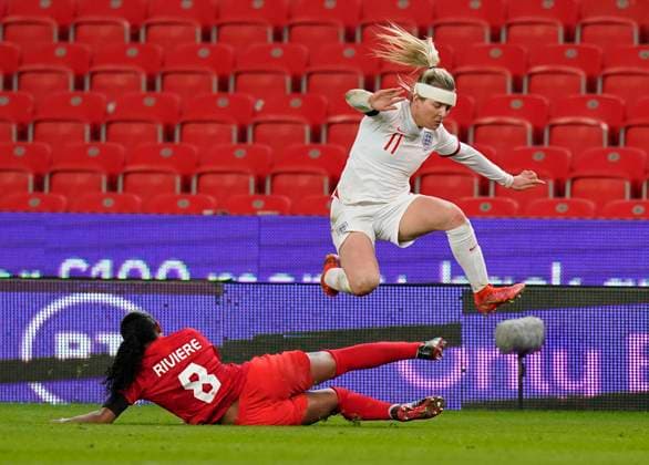 Stoke, England, 13th April 2021. Lauren Hemp of England leaps over a tackle by Jayde Riviere of Canada during the International Football Friendly match at The Bet365 Stadium, Stoke. Picture credit should read: Andrew Yates Sportimage EDITORIAL USE ONLY. No use with unauthorised audio, video, data, fixture lists, club league logos or live services. Online in-match use limited to 120 images, no video emulation. No use in betting, games or single club league player publications. SPI-0999-0038