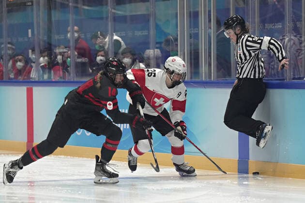 The referee jumps out of the way of the puck as Canadian defender Renata Fast 14 goes up against the boards with Swiss forward Alina Muller 25, in group A of women s Ice hockey, Eishockey at the National Indoor Stadium at the Winter Olympics in Beijing on Thursday, February 3, 2022. Canada dominated the game winning 12-1.  OLY20220203001 RICHARDxELLIS
